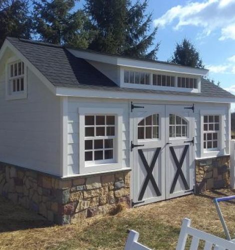 white dormer shed with barn doors, windows, and stone border