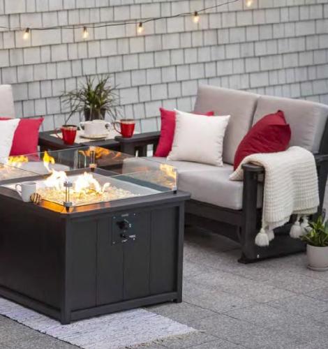 Poly furniture loveseat with tan cushions, white and red throw pillows, and a black base sits in front of a black poly wood fire pit.