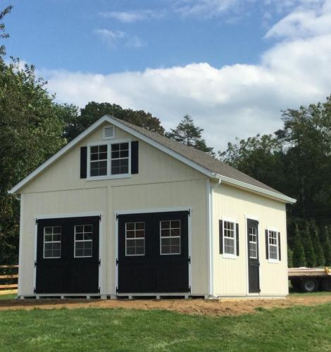 2 Story Doublewide Garage with light yellow siding, white trim, 2 black garage doors, white windows with black shutters, and a black single-entry side door.