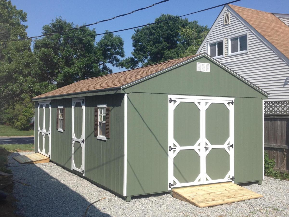 7 foot Cottage Shed with wood siding painted green, white trim, 2 sets of double doors, 1 single entry door, 2 white windows with black shutters, and a brown asphalt roof.