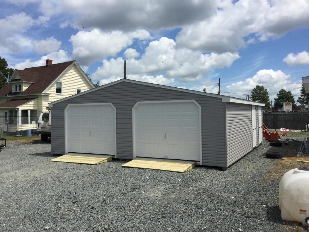 Doublewide Garage with gray vinyl siding, 2 white garage doors, 2 white single-entry side doors, and 2 ramps.