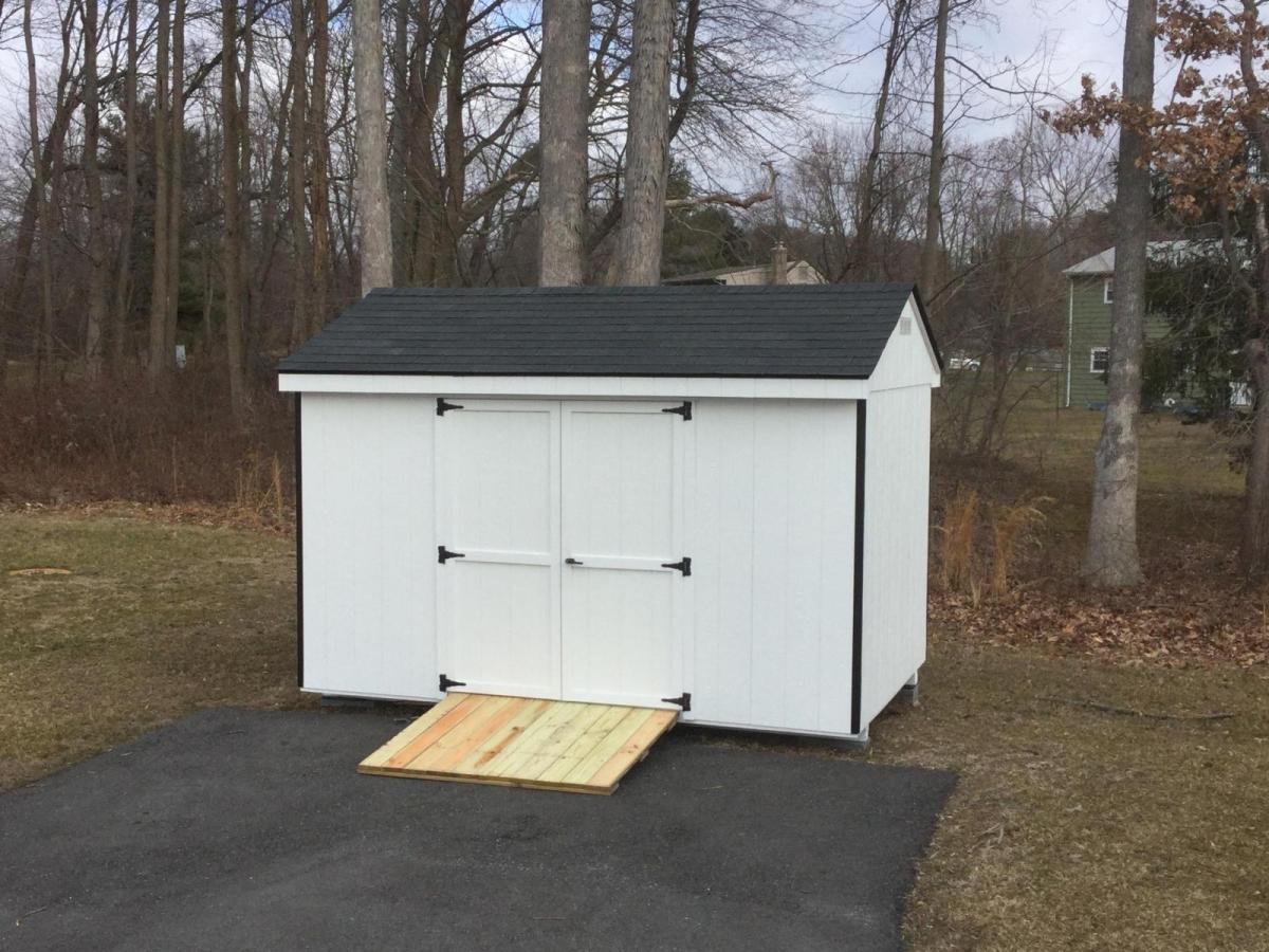 Economy Cottage shed with wood siding painted white, double doors, black trim, a black asphalt roof, and a ramp.