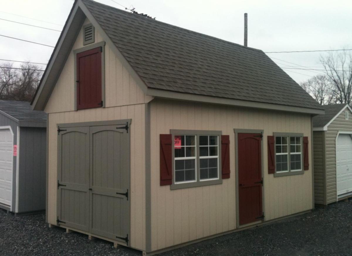 Elite Classic Garden Garage with 2 floors, tan wood siding, taupe trim, taupe double doors, burgundy single-entry door, 2 sets of white windows with taupe trim and burgundy shutters, a brown asphalt roof, and a burgundy loft window.